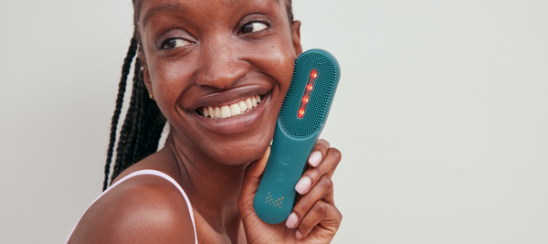 Woman holding MAGNITONE XO Lights Out LED Cleansing Brush next to her face